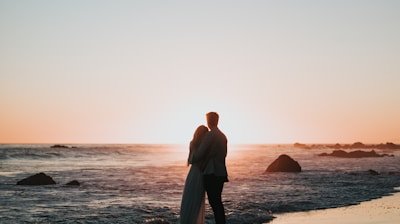 silhouette photo of couple standing on beach watching sunset