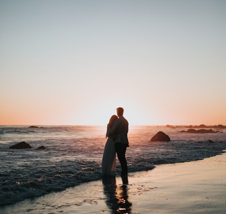 silhouette photo of couple standing on beach watching sunset