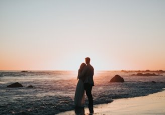 silhouette photo of couple standing on beach watching sunset