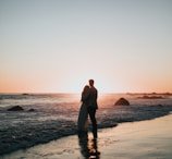 silhouette photo of couple standing on beach watching sunset